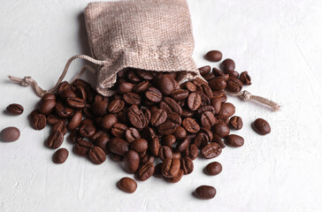 Coffee beans with miniature burlap bag on white concrete background