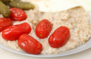 Pickled tomatoes with cucumbers, oatmeal and scrambled eggs. Delicious hearty breakfast, healthy food