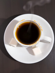 A steaming cup of espresso sits on a saucer, accompanied by two sugar cubes.