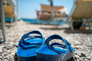 A close-up photo of a pair of summer slippers gently resting on golden beach sand, with soft sea...