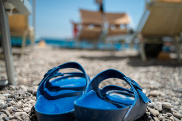 A close-up photo of a pair of summer slippers gently resting on golden beach sand, with soft sea...