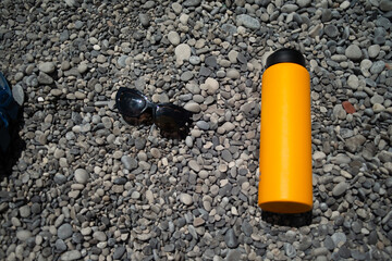 A refreshing summer scene featuring stylish sunglasses and a sleek water flask resting on smooth,...