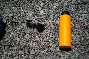 A refreshing summer scene featuring stylish sunglasses and a sleek water flask resting on smooth,...