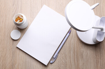 Blank medical journal or notebook with white cover and pills bottle, lamp on table. Mockup for design