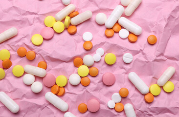 Lots of different pills on pink crumpled paper