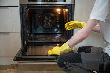 Person cleaning oven door glass with sponge with yellow rubber gloves