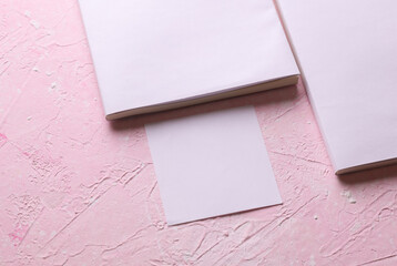 Magazines, sketchbooks or notebooks with white blank covers, memo card on pink concrete background....