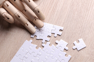 Robotic wooden hand of puppet assembles puzzle on table. Artificial intelligence training concept