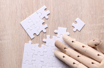 Robotic wooden hand of puppet assembles puzzle on table. Artificial intelligence training concept