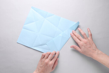 Hands folding blue origami paper on grey background. Top view