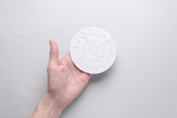 Hand holding white blank assembled round jigsaw puzzle on grey background. Mockup for design