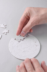 Female hands putting together particles of round white puzzle on grey background