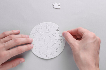 Female hands putting together particles of round white puzzle on grey background