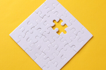 White assembled puzzle without one particle on yellow background