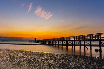 Colorful sunrise by the sea in Italy in Lignano Sabbiadoro, with a pier and lighthouse in the...