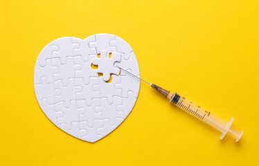 Syringe and white puzzle in the shape of a heart. Diagnosis and treatment of heart diseases. Mockup...