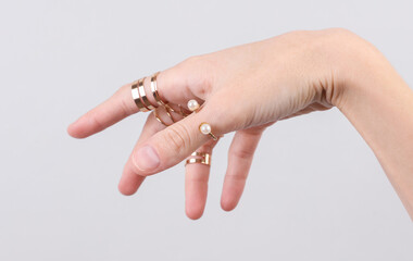 Female hand with many gold rings on fingers, gray background. Beauty concept. Product presentation. Jewelry store