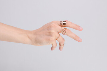 Female hand with many gold rings on fingers, gray background. Beauty concept. Product presentation. Jewelry store