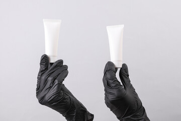 Hands of beautician in gloves holds white empty tubes of cream on gray background. Beauty concept....