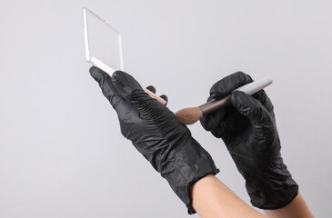 Makeup artist's hands in black gloves holding eye shadow palette with brush
