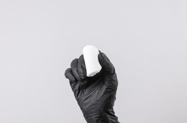 Hand of cosmetologist in a black glove holding a cotton pad on a gray background