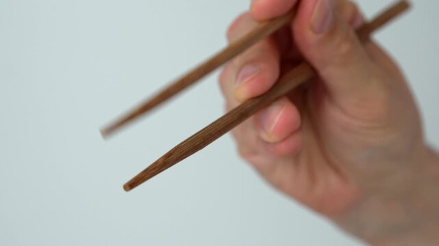 Asian man hands holding bamboo chopsticks for sushi on white background.
Japanese man using bamboo chopsticks to eat traditional Asian food and rolls on white background
