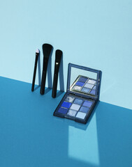 Eye shadow palette with makeup brushes on a blue background with shadow. Creative layout, minimalism