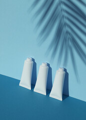 White Cream tubes on a blue background with palm leaf shadow. Mockup. Beauty concept. Creative...