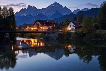 Fototapeta premium Beautiful alpine village with illuminated bridge and houses reflecting in the river at night with the majestic watzmann in the background