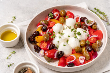 Fresh salad featuring vibrant tomatoes, creamy mozzarella balls, assorted olives, and herbs, served in a rustic bowl with olive oil, showcasing healthy Mediterranean cuisine and colorful ingredients