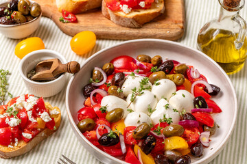 Fresh Mediterranean salad featuring colorful tomatoes, creamy mozzarella balls, olives, and herbs, served in a bowl with toasted bread and olive oil, showcasing vibrant culinary presentation