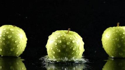 Three green waterdroplet covered apples one suspended in midair against a black background with a reflective surface - Powered by Adobe