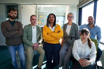Portrait of a diverse team of professionals standing together in a modern office, showing teamwork and collaboration, looking at camera confident.