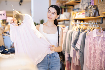 Near clothes rack, girl buys blouse, chooses clothes. Discount season, promotional offers. Style...