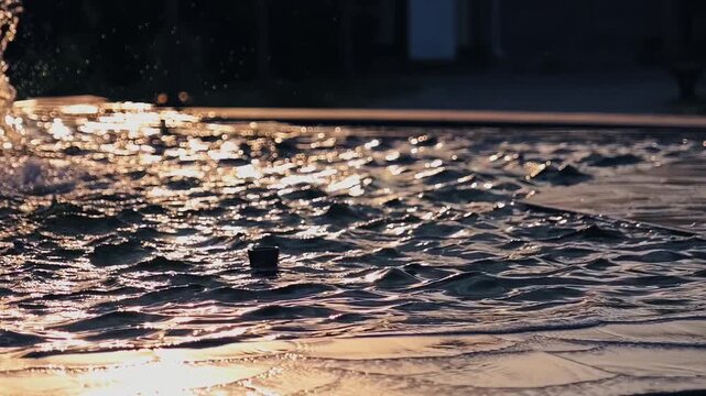 Abstract water surface background: slow motion of water waves in fountain with bokeh during sunset