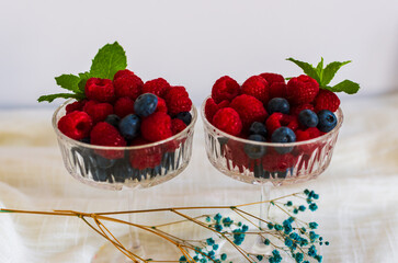 Two glass dessert bowls filled with raspberries and blueberries, decorated with fresh mint....