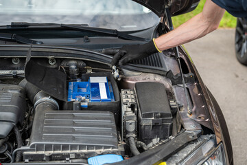 Man connecting car battery terminal with gloved hand during vehicle maintenance