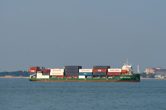 PENANG, MALAYSIA - JUL 06, 2025: Container cargo ship MTT RAJANG transporting stacked shipping containers across calm coastal waters