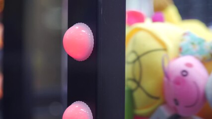 A claw machine with glowing red buttons displays an assortment of colorful plush toys inside. The lively indoor play center environment invites fun and excitement for all ages.