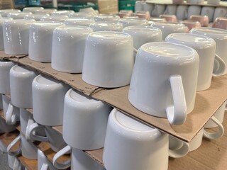 A jumbled pile of numerous white ceramic mugs and cups, some stacked, some scattered, showcasing a...