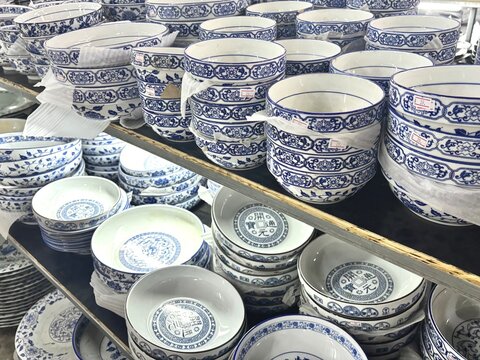 A rich display of traditional blue and white ceramic bowls and plates, adorned with intricate patterns, neatly arranged on shelves in a store, showcasing classic Asian tableware craftsmanship.