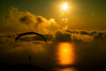 Paraglider soaring over ocean reflecting sunset clouds in breathtaking sky view