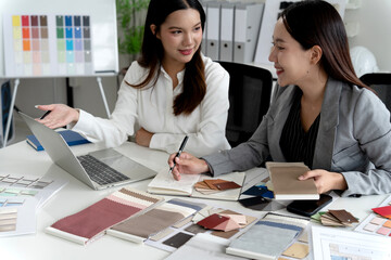 Two Asian female interior designers discussing and examining material