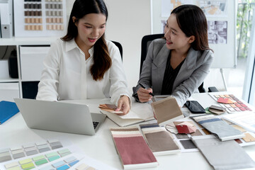 Two Asian female interior designers discussing and examining material