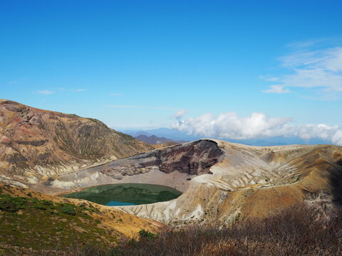 Wide shot of Mount Zao Okama Crater Lake with dramatic volcanic formations and clouds.