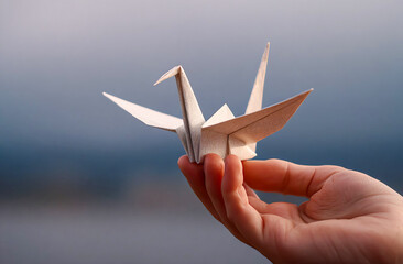 Hand holds a delicate origami crane against a blurred background, showcasing art and craftsmanship. Cultural significance of origami as a symbol of peace and creativity. 