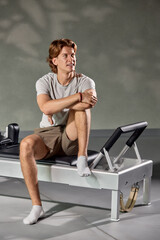 Man seated on a Pilates reformer machine in a fitness studio