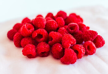 Scattered pile of ripe raspberries on soft pink fabric. Natural light, bright colors, summer fruit...