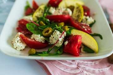 Colorful plate of summer salad with tomatoes, green apples, feta cheese, spinach and olives. Healthy, vibrant and appetizing vegetarian dish.