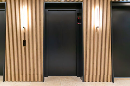 Modern Elevator Lobby Interior. Contemporary Wooden Wall Panels and Black Elevator Doors